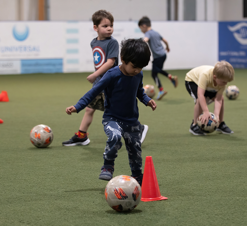 little boy in blue shirt and blue pants dribbling soccer ball