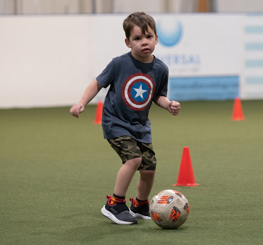 little boy dribbling soccer ball around cones
