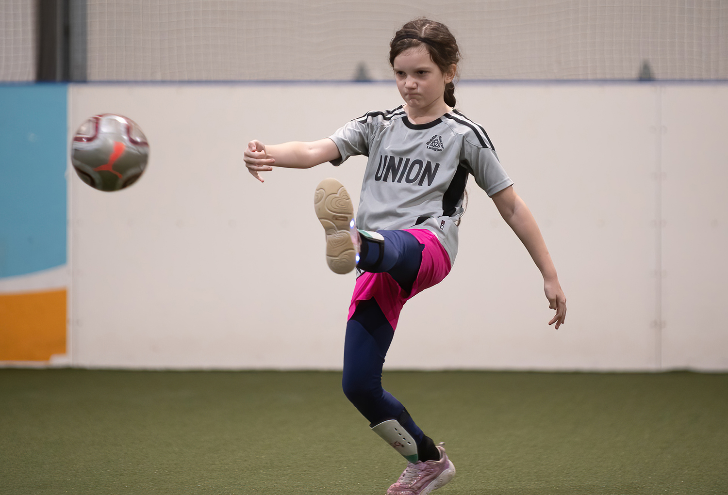 young lady in a gray jersey punts the soccer ball