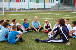young men, soccer players, sit with their coach on field and discuss strategy and soccer fundamentals