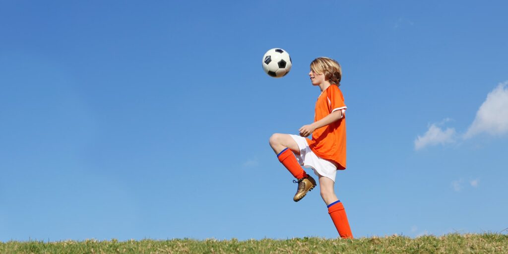 young soccer player juggling a soccer ball against horizon background