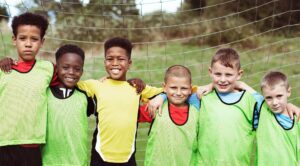 a group of youth soccer players standing in front of open net, wearing scrimmage pinnies.