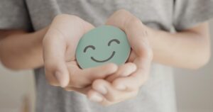 Teen holding a cardboard cutout of a smiley face, symbolizing positive mental health and emotional well-being.