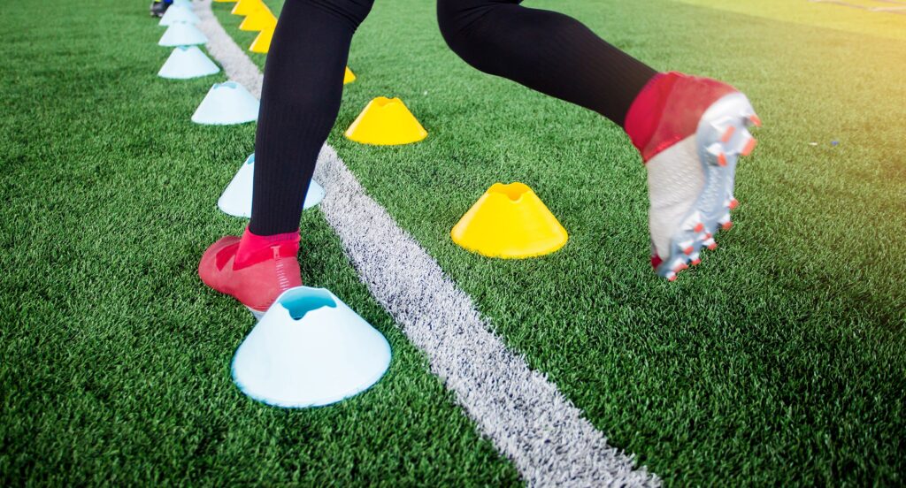 Close-up of a soccer player's feet performing footwork drills through cones during a training session.