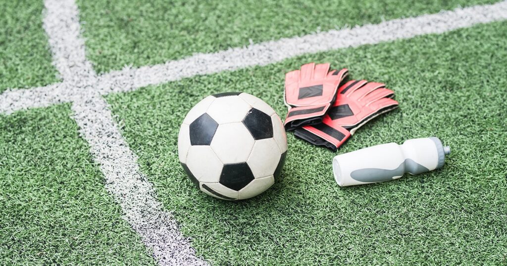 Close-up of a soccer ball, goalie gloves, and a water bottle on an indoor turf field at Locker Soccer Academy in Powell, Ohio.