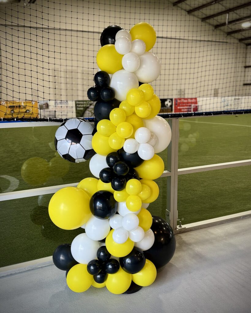 A vibrant black, yellow, and white balloon garland designed for a Locker Soccer party package, perfect for creating a festive atmosphere.