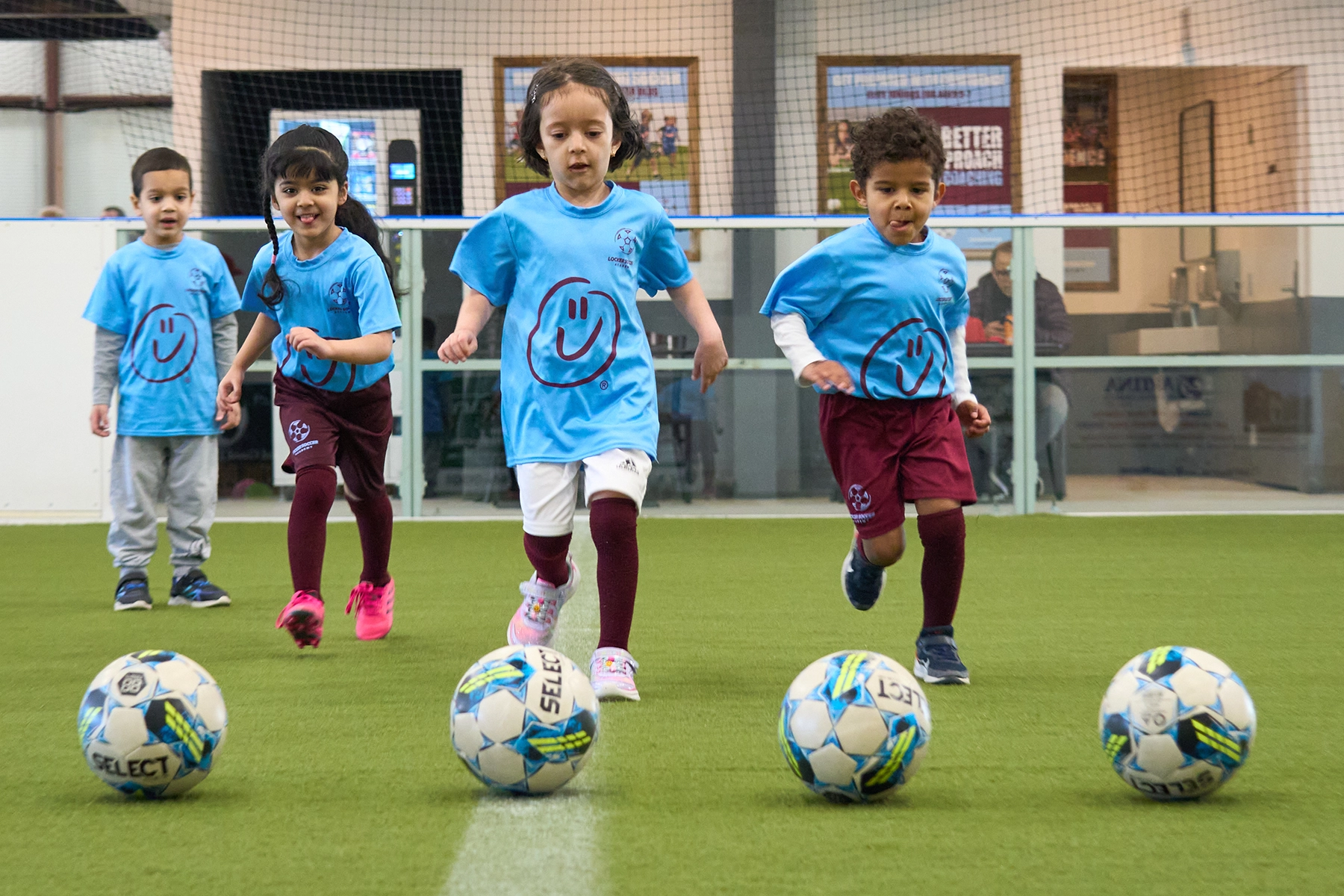 Four young Little Kickers students running toward four soccer balls during a front-view drill at Locker Soccer Academy