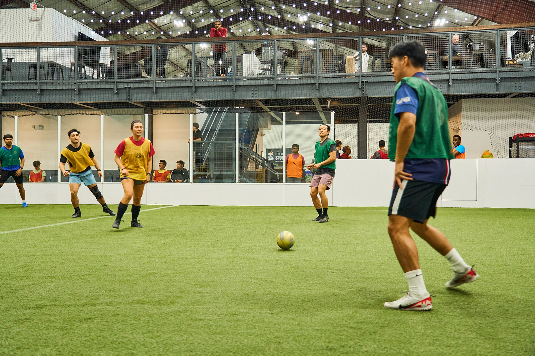 Adult pickup soccer players passing near midfield at Locker Soccer Academy with mezzanine bar in the background