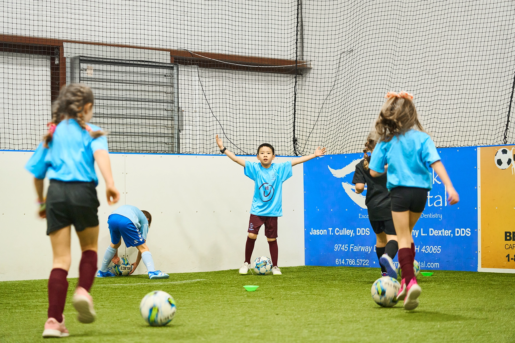 Children in Locker Soccer’s School of Excellence performing a dribbling drill indoors, one child raising arms in celebration after completing drill first