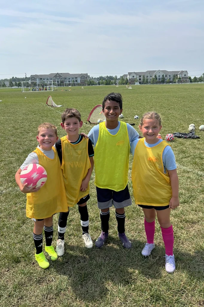 Player Development Camp players wearing yellow scrimmage jerseys smile together during Locker Soccer Academy summer camp