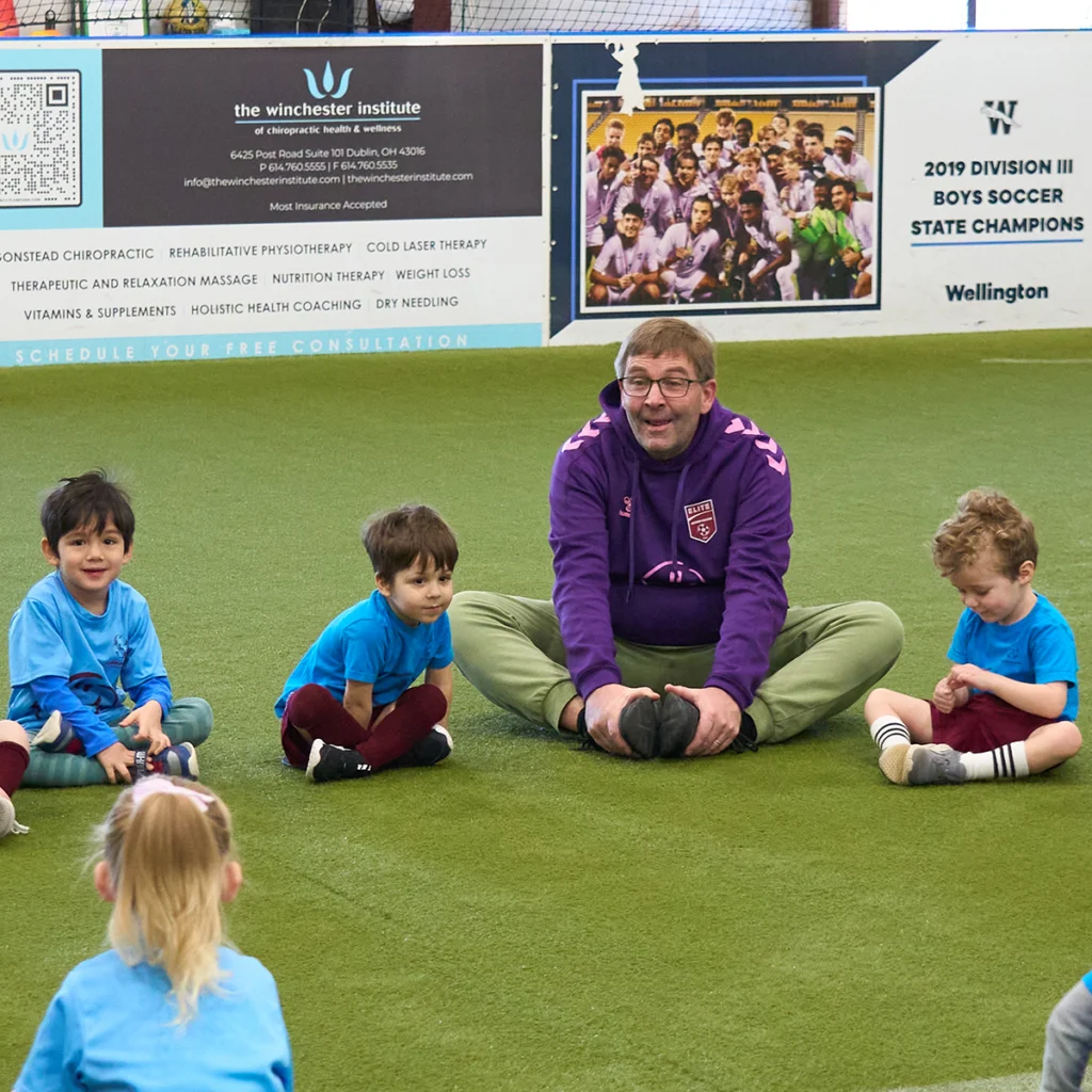 3 year old kids sitting in a circle doing stretch with coach during soccer class in Columbus Ohio