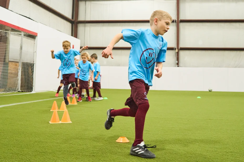Young soccer players weaving through cones during agility running drill