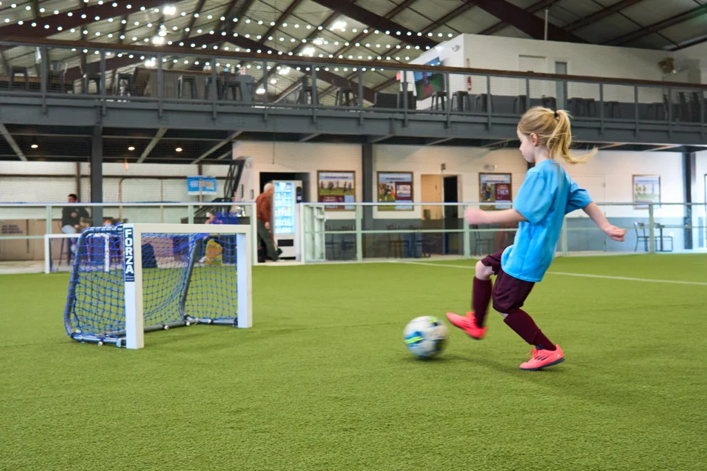 Young girl kicking a soccer ball into a small net during indoor soccer training