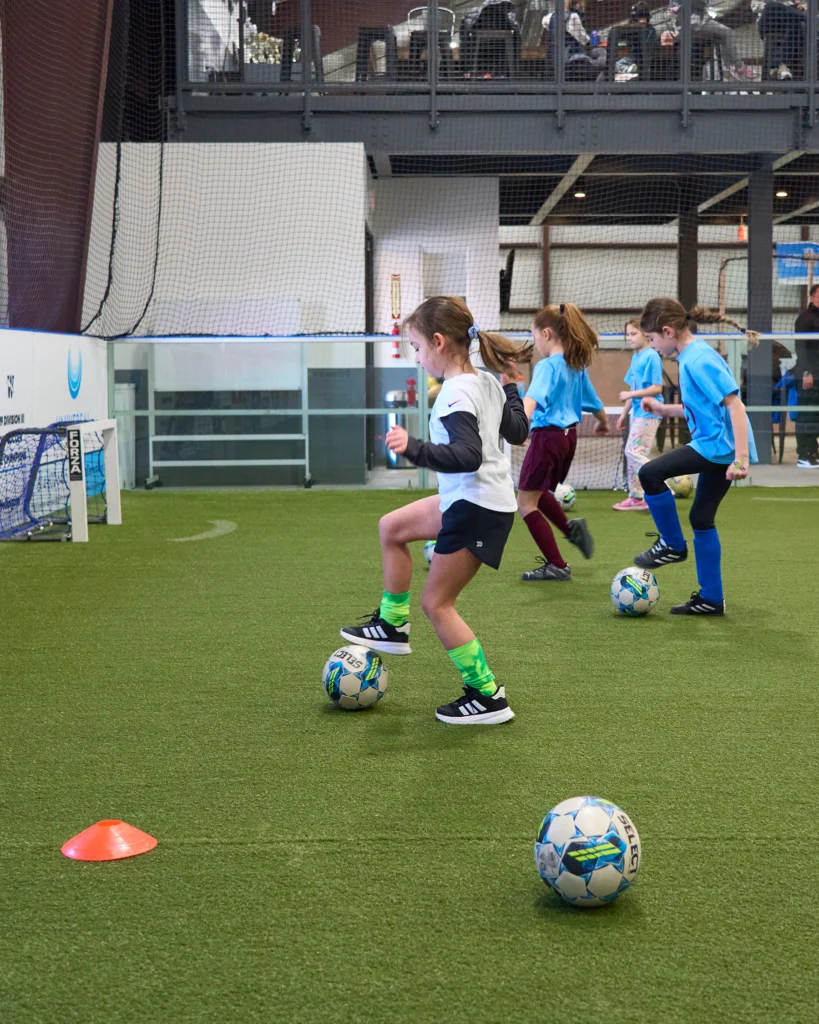 Girls soccer players practicing footwork drills with soccer balls on indoor turf